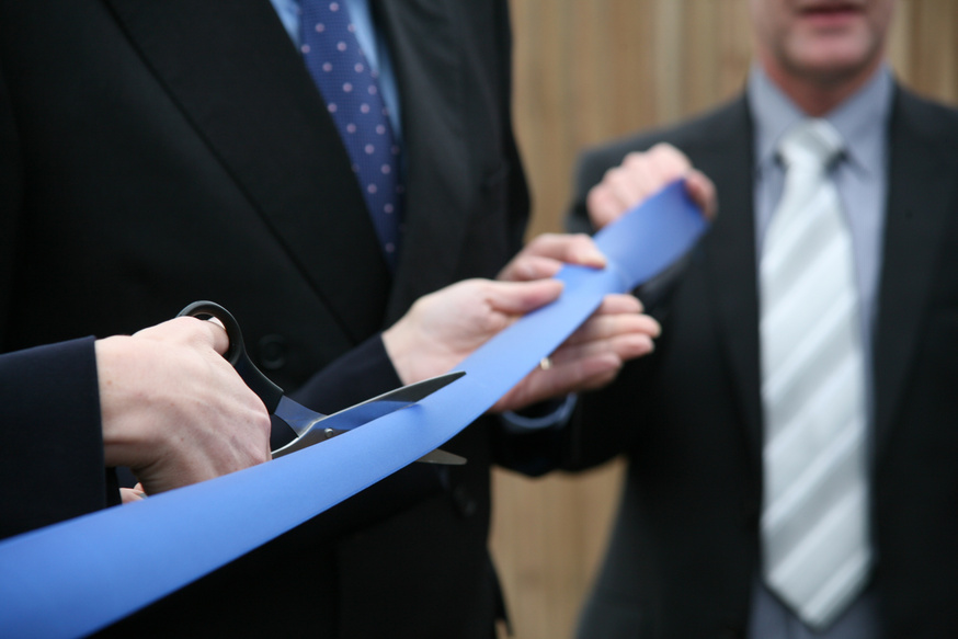 Businessmen in suits holding scissors cutting a blue ribbon